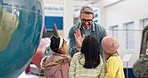 School, children and high five from teacher in class learning about geography, world map and globe with kids together in lesson. Students, group and man with support, praise and success in teaching