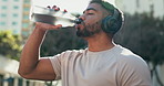 Fitness, man and drinking water with headphones outdoor for sports break, energy and workout. Thirsty indian runner, bottle and hydration of nutrition, healthy recovery and listening to music in city