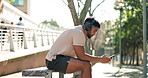 Man, bench and phone for music with headphones in city for a workout, exercise or training. Athlete person sit outdoor on break or rest with a smartphone, internet and listening to audio and typing