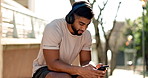 Bench, man and phone for music with headphones in city for a workout, exercise or training. Athlete person sit outdoor on break or rest with a smartphone, internet and listening to audio and typing