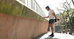 Man, stretching and exercise with music headphones in city for a workout or training. Athlete person outdoor on urban street for legs warm up, streaming and listening to audio for performance and run