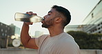 Fitness, man and drinking water in city for sports break, energy and workout performance. Thirsty athlete, indian runner and bottle for hydration, nutrition and healthy recovery of outdoor exercise 