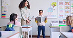 Student, child and reading a book in class for learning, development and communication. A boy kid and teacher woman teaching language, support and assessment in elementary classroom at school