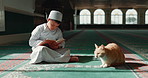 Quran, islamic and child in a mosque for praying, peace and spiritual care in holy religion for Allah. Reading book, Ramadan or Muslim kid with a cat animal, hope or gratitude to study or worship God