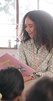 Reading, kids and teacher with book at school storytelling, learning or child development in kindergarten. Group, education or African woman teaching students fun language story in classroom together
