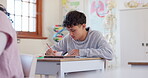 School, exam and a boy student writing in class during a test or assessment learning or development. Education, kids and a male child at a classroom desk for academic study or scholarship assignment