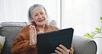 Tablet, video call and senior woman on a sofa in the living room talking and waving for greeting. Digital technology, happy and elderly female person on a virtual conversation in the lounge at home.