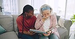 Photo album, assisted living and a senior laughing with her black woman caregiver on a sofa in the living room. Smile, funny and elderly resident looking at a memory with a nurse in a retirement home