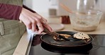 Cooking, closeup and woman frying pancakes in a pan on a stove in the kitchen of her home. Baking, dessert and female person or chef preparing chocolate crepes for a sweet breakfast meal or snack.