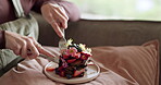 Woman, hands and eating cake for breakfast on birthday, morning in home to relax in living room with food. Cutting, knife and fork or person with dessert for meal on sofa in house on holiday or break