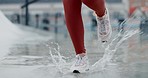 Person, legs and running in water splash, fitness or outdoor workout for cardio exercise or training. Closeup of active runner or athlete stepping on puddle in sprint, marathon or sports motivation