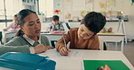 Education, support and teacher help child in class with school work, writing and assessment in a classroom. Teaching, together and kid learning to answer test or exam in notebook as knowledge at desk