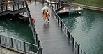 Walking, above and women on a bridge during rain for nature bonding, vacation or weekend together. Talking, lake and friends or young people with an umbrella in winter for water on a boardwalk