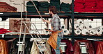 Tablet, leather workshop and man on ladder at shelf for fabric choice. Tech, craftsman and person select tannery textile in factory for production, manufacturing and work on steps in small business