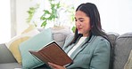 Notebook, reading and Asian woman on a sofa in the living room to relax, reflect and journal at home. Calm, happy and young female person writing notes in a book in the lounge of modern apartment.