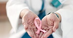 Hands, medical and a pink ribbon for breast cancer with a doctor in a hospital closeup for support or empathy. Healthcare, hope and awareness month with a confident medicine professional in a clinic