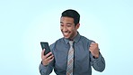 Business man, phone and celebration in studio, winner and fist in air for prize, giveaway or goal by blue background. Entrepreneur, trader and smartphone for fintech, profit or bonus on stock market