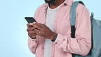 College student, hands and typing on a phone for communication or chat in studio. Closeup of a person with a backpack and smartphone for writing email, network and social media on a blue background
