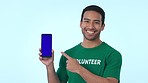 Blue screen, cellphone and man volunteer pointing to mockup space for marketing, promotion or advertising. Tracking markers, phone and portrait of Indian male community worker by studio background.