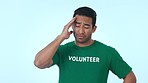 Volunteer, headache and stress of a man in studio for community service, charity and social welfare. Frustrated or tired asian person on a blue background with pain, depression or volunteering crisis