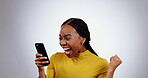 Woman, surprise and phone for winning in studio to celebrate success, mobile news or bonus giveaway promotion on grey background. Excited african model, smartphone or fist to cheers for lottery prize