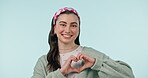 Face, heart and hands of woman in studio for peace, kindness and charity donation on blue background. Portrait, happy model and finger shape of hope, love and thank you for support, emoji and sign 
