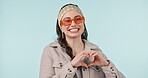 Happy, face and studio woman with heart hands for kindness, support and clothing satisfaction, care and love. Emoji icon gesture, fashion style and portrait of person with glasses on blue background