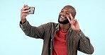 Peace, sign and man in selfie for video call on social media, blog or mockup with phone on studio blue background. Influencer, emoji and smile for live streaming, chat and profile picture on vlog