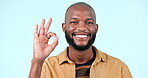 Ok, hand and portrait of man with thank you, emoji or happy feedback on blue background in studio with support. Agreement, gesture and review with yes, like or face with smile and praise or promotion