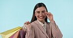 Face, glasses and happy woman with shopping bag in studio isolated on a blue background. Fashion portrait, customer smile and gifts on discount, sales and purchase at boutique, mall and retail store.