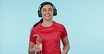 Face, fitness and a woman running with music, sweating and water for hydration on a blue background. Smile, tired and portrait of an athlete or runner with a bottle, headphones audio and exercise