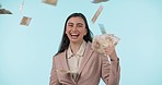 Happy, lottery and raining money with a woman winner in studio on a blue background for financial freedom. Portrait, smile and a rich or wealthy person looking confident with finance or accounting