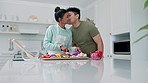 Cooking, couple and kiss with kitchen, flower surprise and food with happy and gift at home. Smile, young people together and helping with lunch in a house with recipe, ingredients and preparation