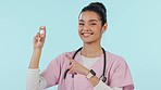 Woman is pointing at vaccine bottle, nurse in studio and yes to medicine for safety from virus on blue background. Promotion, medical advice and agreement with immunization, portrait and healthcare
