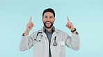 Doctor, man and pointing up for healthcare presentation, clinic news and happy information in studio. Face of medical professional marketing, choice and steps, guide or advice on a blue background