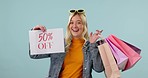 Offer, face or happy woman with shopping bag from sale or clothes on promotion on blue background. Smile, portrait or excited gen z girl customer in studio with fashion product on discount sign 