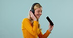 Dance, smartphone or happy woman in studio listening to music for freedom on blue background. Smile, headphones or gen z girl singer streaming radio song, sound or audio on web or online mobile app