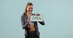 Open sign, woman and face with gym, entrepreneur and startup poster in a studio. Blue background, female person and portrait with a smile and notice of a fitness or workout shop with billboard
