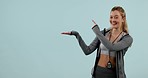 Fitness, smile and woman pointing at hand in studio isolated on a blue background. Portrait, palm advertising and marketing workout of coach or sports promotion of personal trainer on mockup space.
