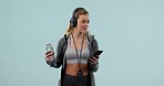 Fitness, phone and a woman with water and headphones for streaming and dancing in studio. Athlete person with a smartphone and listening to music or audio for sports workout on a blue background