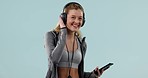 Woman at gym, headphones and smartphone, listening to music and dancing for fitness and mockup space in studio. Happy, energy and exercise, personal trainer using phone and radio on blue background