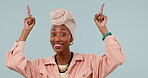 African woman, portrait and pointing up in studio for announcement, advertising or smile. Face of black female person with a turban and hand gesture on blue background for presentation or choice