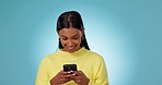 Woman, smile and typing with phone in studio, scroll social media or reading notification on blue background. Happy indian model download digital app, mobile games online or search meme on smartphone