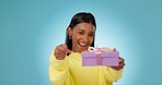 Woman, smile and pointing at gift in studio for birthday present, retail sale or product deal on blue background. Indian person, giveaway winner and excited for ribbon box, promotion or celebration