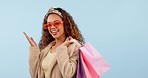 Fashion, shopping and excitement with a woman customer in a princess tiara on a studio blue background. Portrait, smile and retail with a happy young person carrying bags for a sale or discount