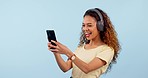 Woman, scroll social media with headphones and smartphone in studio, funny meme and typing in chat. Comedy online, using phone and mobile app with mockup space, music or radio on blue background