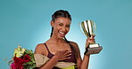 Champion, trophy and bouquet, woman with celebration in studio for sports achievement and winning on blue background. Happiness, portrait and cheers at fitness event, award or prize with flowers