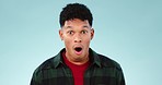 Face, wow and surprised with the reaction of a man in studio on a blue background looking shocked at news. Portrait, alarm and mind blown with a young person hearing a secret, announcement or gossip