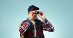 Binocular, hiking and travel with man, wellness and bird watching on a blue studio background. Person, model and traveller with wildlife, view or fitness with sightseeing, environment or backpacking