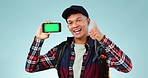 Face, green screen and man with smartphone, thumbs up and backpacker on a blue studio background. Portrait, hiker and person with a cellphone, tracking markers and hand gesture with support and smile